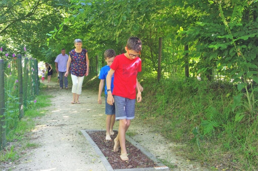 Deux garçons traversent un sentier sensoriel pieds nus, ressentant les textures naturelles sous leurs pas.