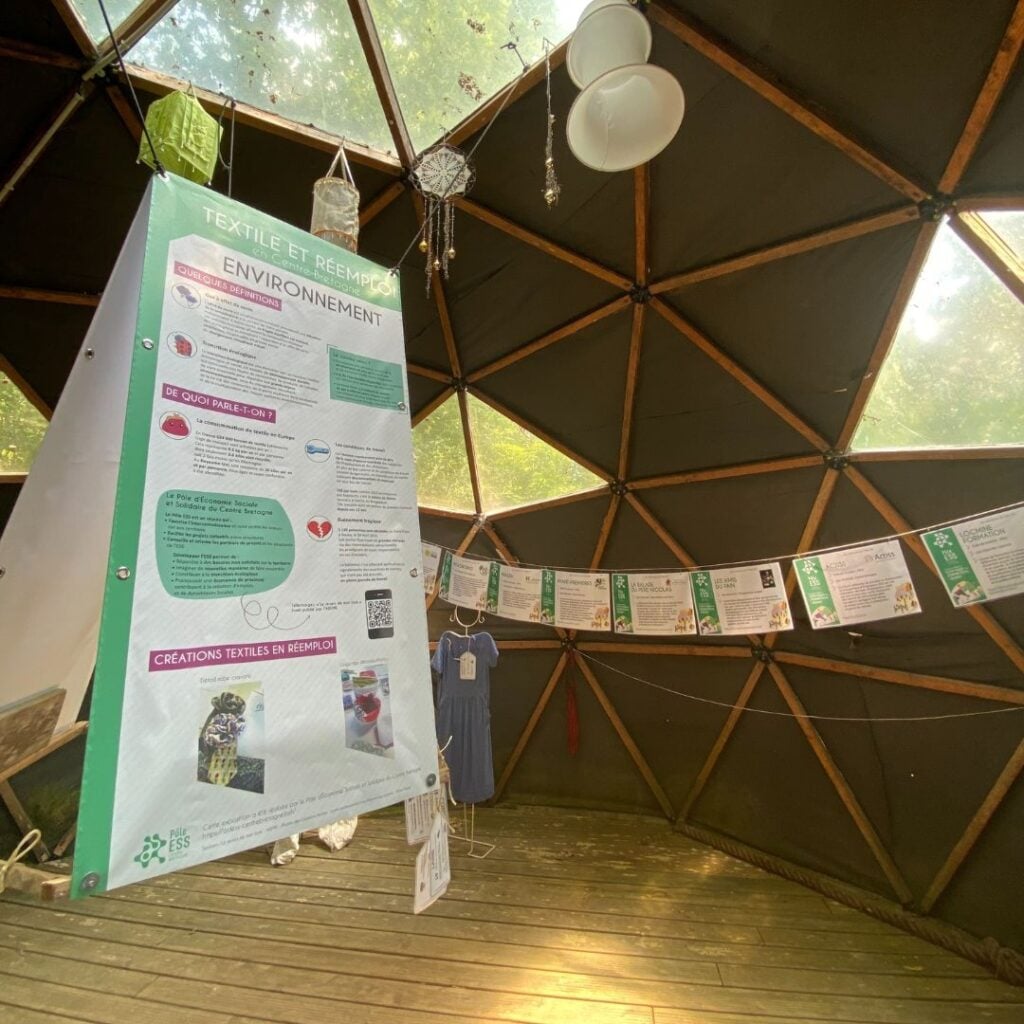 Vue intérieure d'un dôme géodésique, mettant en avant des panneaux explicatifs sur le textile et le réemploi, avec des créations textiles exposées dans un cadre immersif.