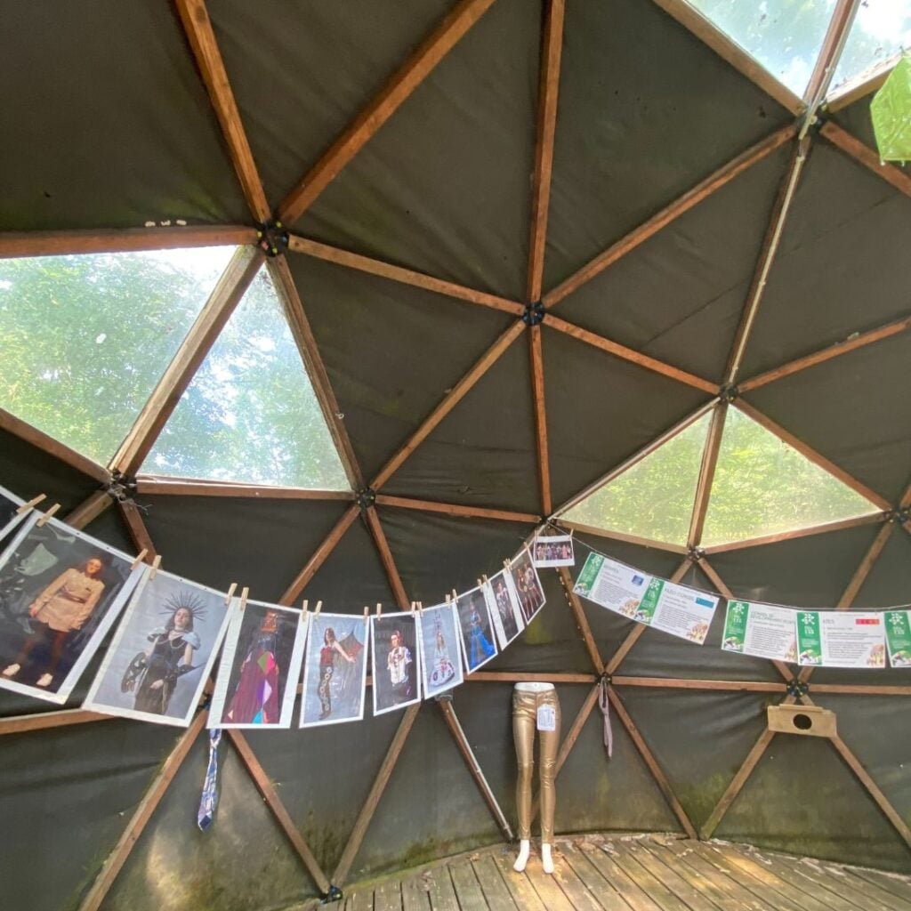 Vue intérieure d'un dôme géodésique, présentant une exposition avec des photos suspendues et des explications sur le textile et l'environnement, dans un cadre éducatif et artistique.