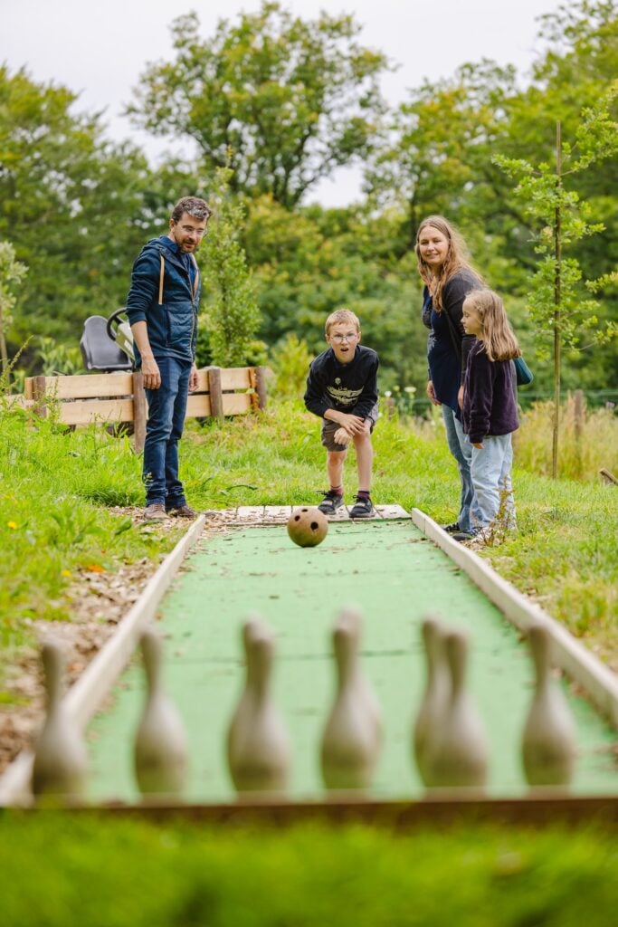 La joie partagée d'une partie de bowling en plein air, avec un garçon lançant la boule tandis que sa famille sourit derrière lui."