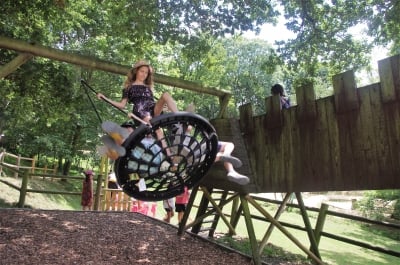Une jeune fille se balance sur une balançoire en forme de nid, entourée par un cadre verdoyant et naturel.