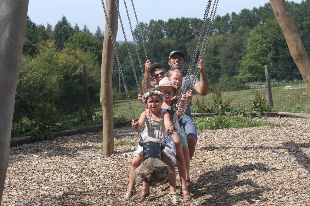 Une famille partage un moment complice sur une balançoire à cordes, avec plusieurs enfants assis devant et un adulte les poussant joyeusement.
