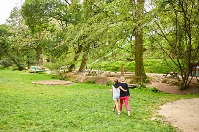 Deux enfants marchant bras dessus bras dessous dans un cadre verdoyant, entourés d'arbres et de sentiers, offrant une ambiance paisible et conviviale au cœur de la nature.