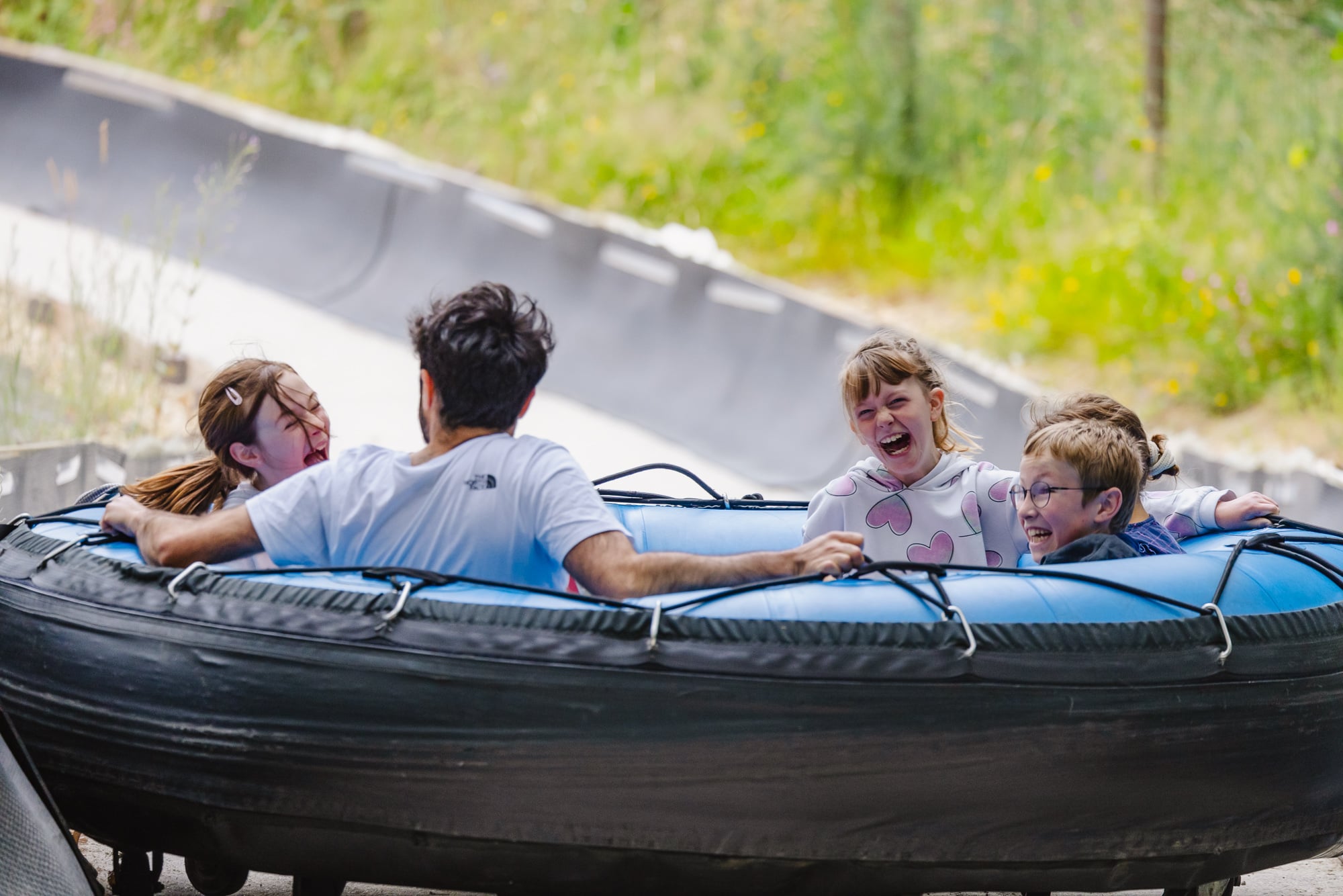Un groupe composé d'enfants et d'un adulte partage un moment de rires et de sensations fortes dans une grande bouée circulaire, en train de descendre une piste à vive allure. Les visages des enfants expriment joie et excitation, créant une scène conviviale et pleine d'énergie.